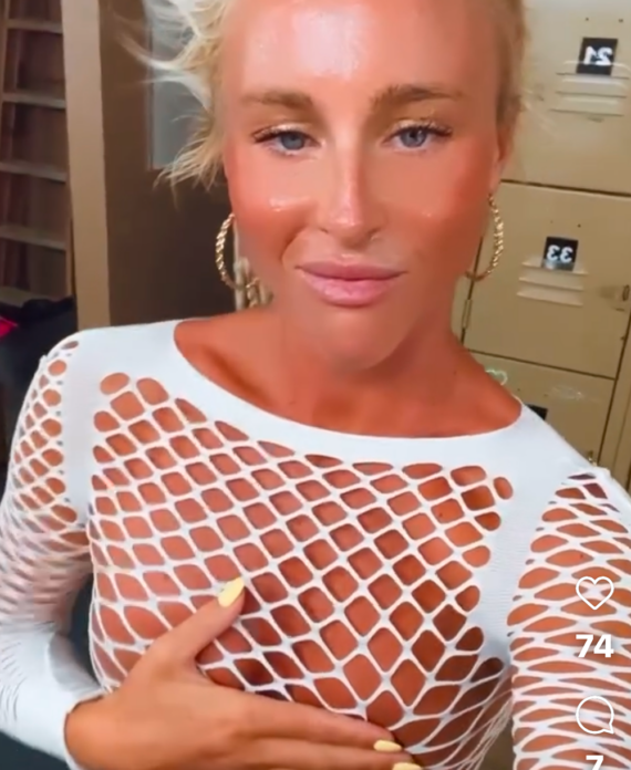 Woman in a white fishnet mesh top posing lockers in the background hand resting on her chest