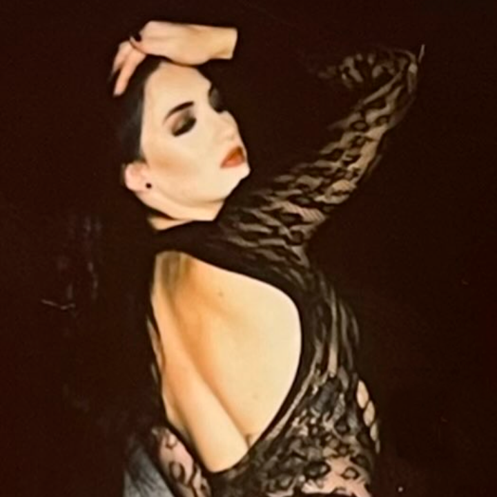 Glamorous portrait of a woman in a black lace dress pale makeup dark hair posed with one arm raised over her head
