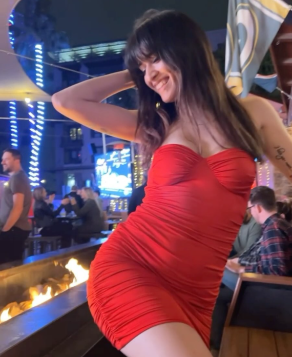 Woman in a red strapless dress posing by a lit fire pit at an outdoor night venue, smiling.** Note: this line seems off; I will correct.