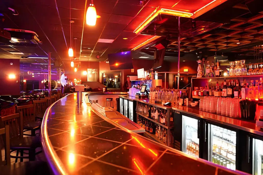 Curved glossy bar in a dim neon lit nightclub with rows of liquor bottles and warm orange lighting
